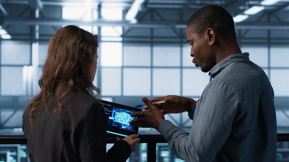 Data center system administrators using artificial intelligence neural networks tech on tablet. Teamworking server farm employees using AI programming language on device screen, camera A